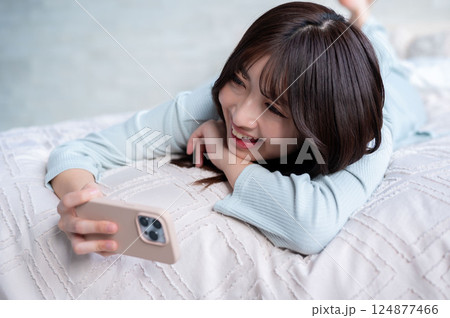 うつ伏せでスマホを操作する若い女性 うつ伏せでスマホを操作する若い女性 124877466