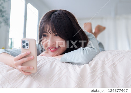 うつ伏せでスマホを操作する若い女性 うつ伏せでスマホを操作する若い女性 124877467