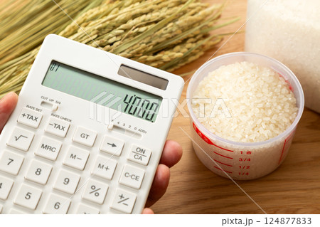 計量カップに入った米と電卓を持つ手元 124877833