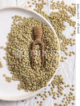 Plate full of dried raw green lentils with a wooden scoop on white table top view. Vegetarian food Plate full of dried raw green lentils with a wooden scoop on white table top view. Vegetarian food 124877986
