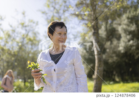 Elderly woman holding wildflowers enjoying sunny day in park 124878406