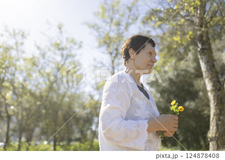 Elderly woman holding flowers enjoying sunny day in park 124878408