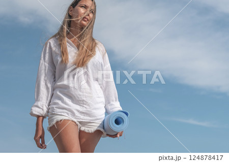 Woman walking on beach holding yoga mat in summer 124878417