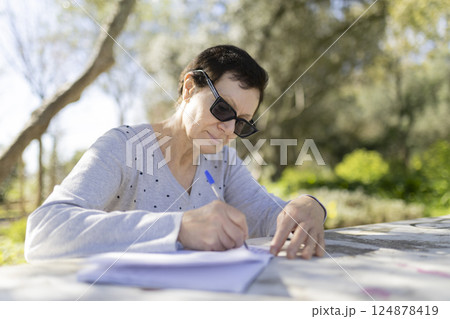 Senior woman writing outdoors in a park on a sunny day 124878419