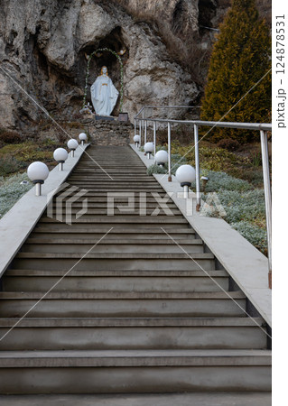 Steps lead to a serene statue of a figure in a natural cave setting surrounded by greenery and soft lighting 124878531