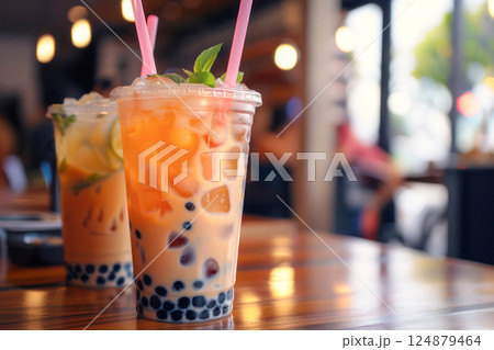 Colorful bubble tea drinks in clear cups, garnished with fresh mint, presented on a counter with a warm bokeh light background. 124879464