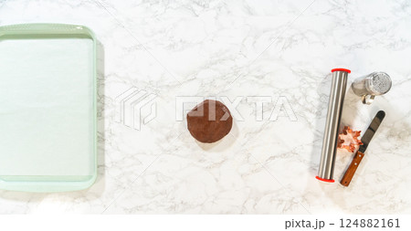Overhead view of ingredients and tools, including chocolate cookie dough and snowflake-shaped cutters, set on a white marble surface for making Chocolate Ginger Sugar Cookies. 124882161