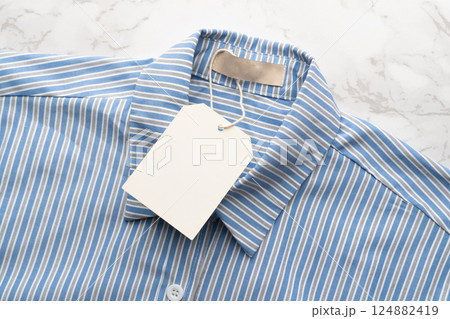 Blue striped shirt with blank tag label on marble background. Mock up for design. Blue striped shirt with blank tag label on marble background. Mock up for design. 124882419
