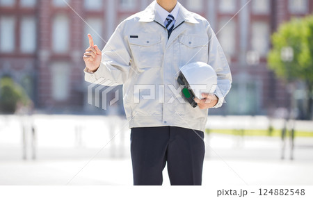 ヘルメットを抱え指差しをする作業服の若い男性 124882548