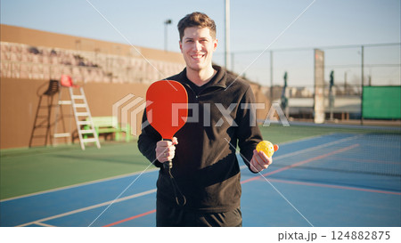 Portait of a young, happy and smiling man holding pickleball paddle Portait of a young, happy and smiling man holding pickleball paddle 124882875