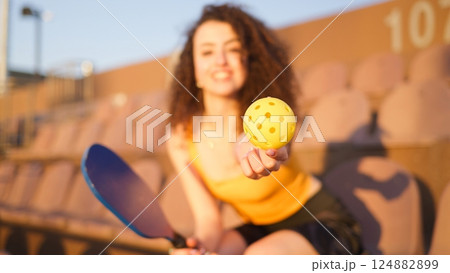 Portrait of young girl adult posing with pickleball paddle and ball on stadium chairs 124882899