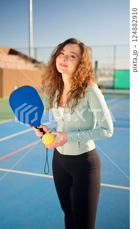Portait of a young, happy and smiling curly haired girl holding pickleball paddle Portait of a young, happy and smiling curly haired girl holding pickleball paddle 124882910