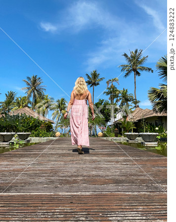 Woman in red long dress walking over a wooden way on tropical resort at sunny day Woman in red long dress walking over a wooden way on tropical resort at sunny day 124883222