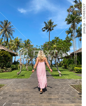 Woman in red long dress walking over a wooden way on tropical resort at sunny day Woman in red long dress walking over a wooden way on tropical resort at sunny day 124883227