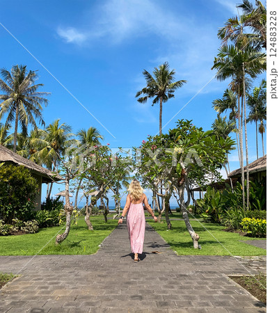 Woman in red long dress walking over a wooden way on tropical resort at sunny day Woman in red long dress walking over a wooden way on tropical resort at sunny day 124883228