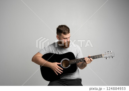 Bearded guitarist man with a black guitar playing a song in a studio white background. Bearded guitarist man with a black guitar playing a song in a studio white background. 124884933