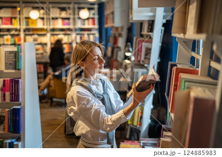 Thoughtful woman customer chooses and reads books from shelves in bookshop. Book worm and read hobby 124885983