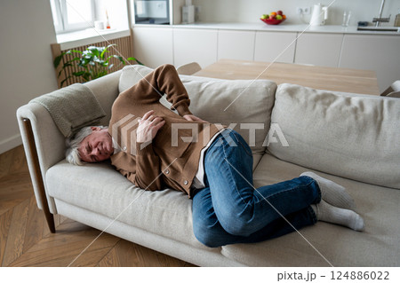 Exacerbation of hernia. Struggling old man curled in back pain on couch suffer from osteochondrosis Exacerbation of hernia. Struggling old man curled in back pain on couch suffer from osteochondrosis 124886022