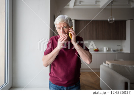 Scared stressed old man grips phone tightly, hearing urgent financial request from fraud stranger Scared stressed old man grips phone tightly, hearing urgent financial request from fraud stranger 124886037
