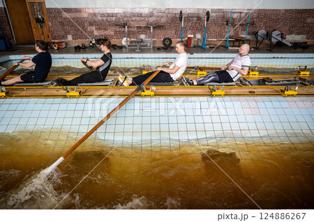 Focused determined athletes refine synchronized rowing, mastering oar control on simulator in pool Focused determined athletes refine synchronized rowing, mastering oar control on simulator in pool 124886267
