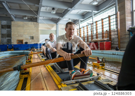 Fatigued focused athletes train rigorously on rowing simulator in gym pool pushing past exhaustion 124886303