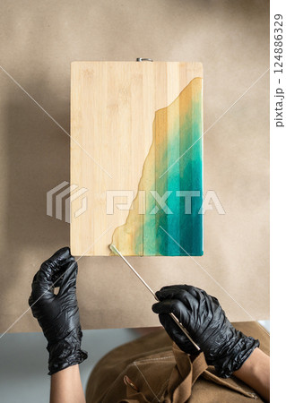 Hands of artist work with epoxy resin pigment spread on board. Intricate design gradient. Top view 124886329