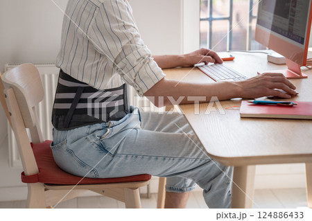 Man works on computer wears back support belt on lower back to relieve stress on spine has hernia. Man works on computer wears back support belt on lower back to relieve stress on spine has hernia. 124886433