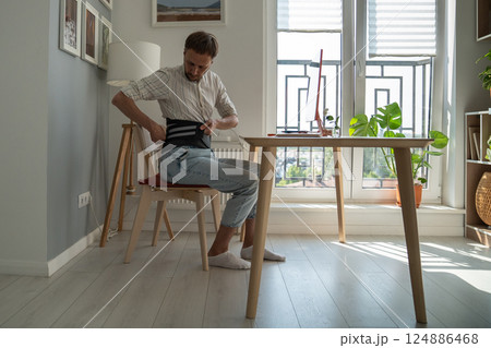 Man fixing belt corset before starting work to ease load on spine after an exacerbation hernia. Man fixing belt corset before starting work to ease load on spine after an exacerbation hernia. 124886468