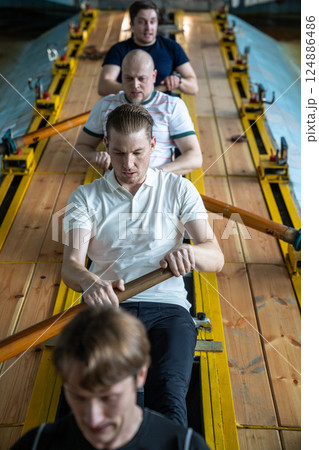 Top view exhausted determined rowers push limits training intensely on rowing simulator in gym pool 124886486