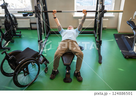 Disabled athlete strengthens body by lifting barbell in gym, healthy sports for physical progres Disabled athlete strengthens body by lifting barbell in gym, healthy sports for physical progres 124886501