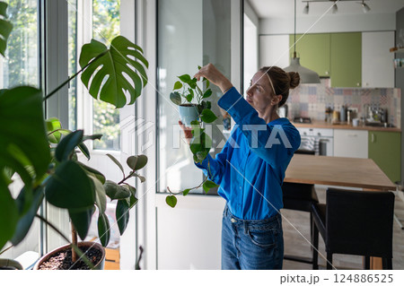 Enthusiastic middle aged woman inspects Philodendron leaves at home. Hobby for mental health.  124886525