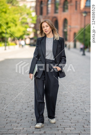 Stylish female entrepreneur with laptop stroll through urban streets, digital nomad and freelancer 124886529