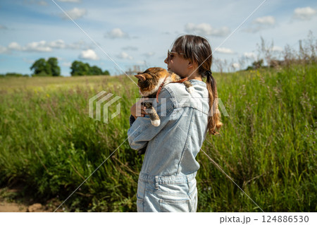 Side view of woman hugging calm peaceful cat tightly while walking in rural countryside nature area. Side view of woman hugging calm peaceful cat tightly while walking in rural countryside nature area. 124886530