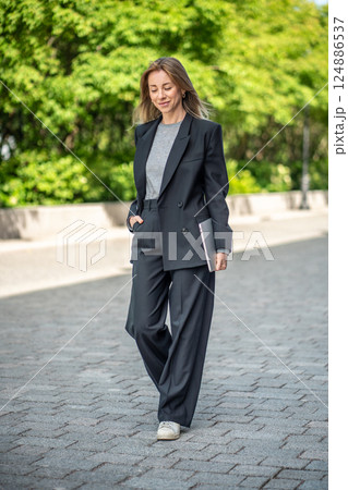 Smiling cool businesswoman strolling outdoors with laptop, balancing work and life on the go 124886537