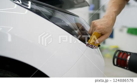 Professional applying protective film on car headlight 124886576