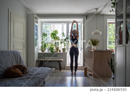 Rearview woman with arms clasped and raised in stretching pose, warm up energy exercise in morning 124886593