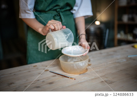 Female potter carefully apply glaze from jug to ceramic plate in pottery workshop. Artistic job, DIY Female potter carefully apply glaze from jug to ceramic plate in pottery workshop. Artistic job, DIY 124886633