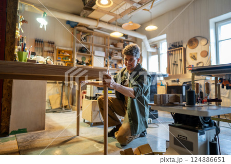 Woodworker reviews table assembly, satisfied with outcome in carpentry workshop. Furniture design 124886651