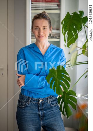 Calm happy woman standing close to mini garden by monstera leaves at home or office, plant care 124886681