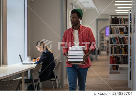 Student with huge stack of educational books goes to library workplace to prepare for entrance exams Student with huge stack of educational books goes to library workplace to prepare for entrance exams 124886704