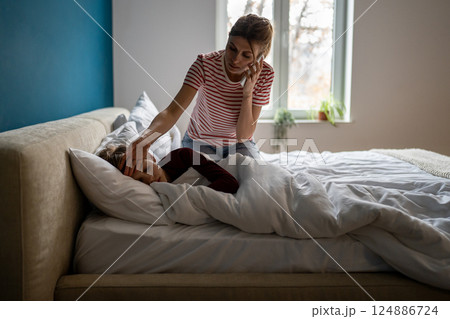 Worried young woman mother calling to pediatrician while measuring son temperature at home Worried young woman mother calling to pediatrician while measuring son temperature at home 124886724