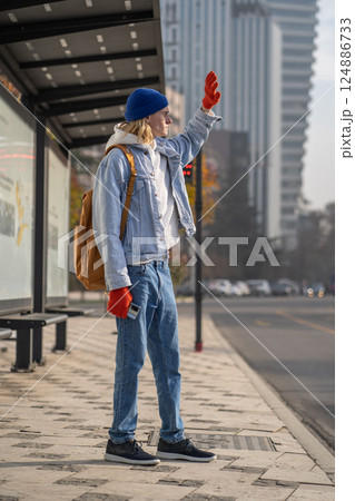 Young guy traveler at bus stop waiting for transport covered with hand from scorching sun. 124886733