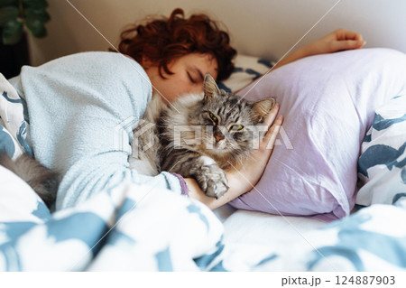sleeping young woman on bed with pet cat 124887903