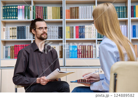 Young male psychologist, college worker counseling teenage student girl in library, office Young male psychologist, college worker counseling teenage student girl in library, office 124889582