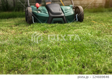 Gardening work tools. Green electric aerator scarifier for soil cultivation and compaction on bright lush green lawn grass. Professional lawn care service. Grass maintenance. Place for text. Gardening work tools. Green electric aerator scarifier for soil cultivation and compaction on bright lush green lawn grass. Professional lawn care service. Grass maintenance. Place for text. 124889646