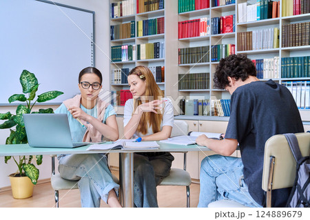 Group of students teenagers sitting together at desk in library preparing for tests exams Group of students teenagers sitting together at desk in library preparing for tests exams 124889679