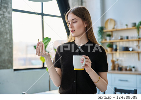 Young beautiful woman taking capsule with fish oil Omega 3, at home 124889689