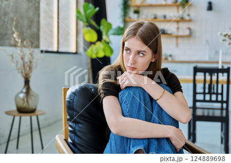 Sad unhappy thoughtful young woman sitting in armchair at home 124889698