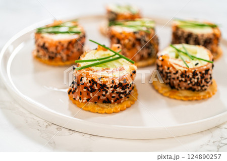 A beautifully plated presentation of smoked salmon jumbo cream cheese rolls on a round white plate. Each roll is sliced to reveal the creamy filling, accented by cucumber slices and wrapped in smoked A beautifully plated presentation of smoked salmon jumbo cream cheese rolls on a round white plate. Each roll is sliced to reveal the creamy filling, accented by cucumber slices and wrapped in smoked 124890257