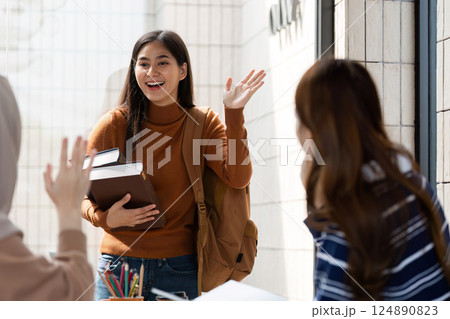 Student Arrival and Greeting. A student enters a cafe, greeting friends with enthusiasm and books in hand. 124890823